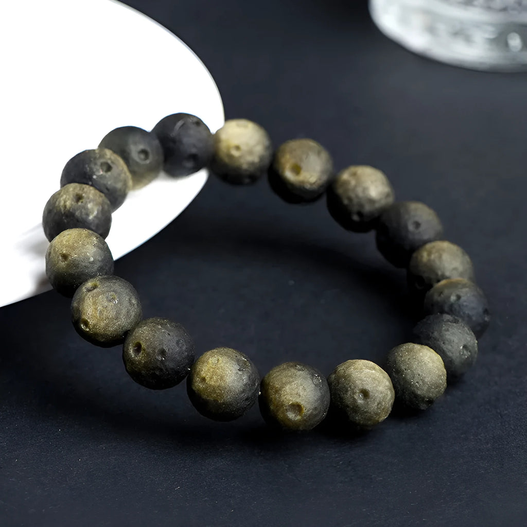 Natural obsidian crater ball bracelet in gold or silver finish on a wrist, showing textured bead detail.