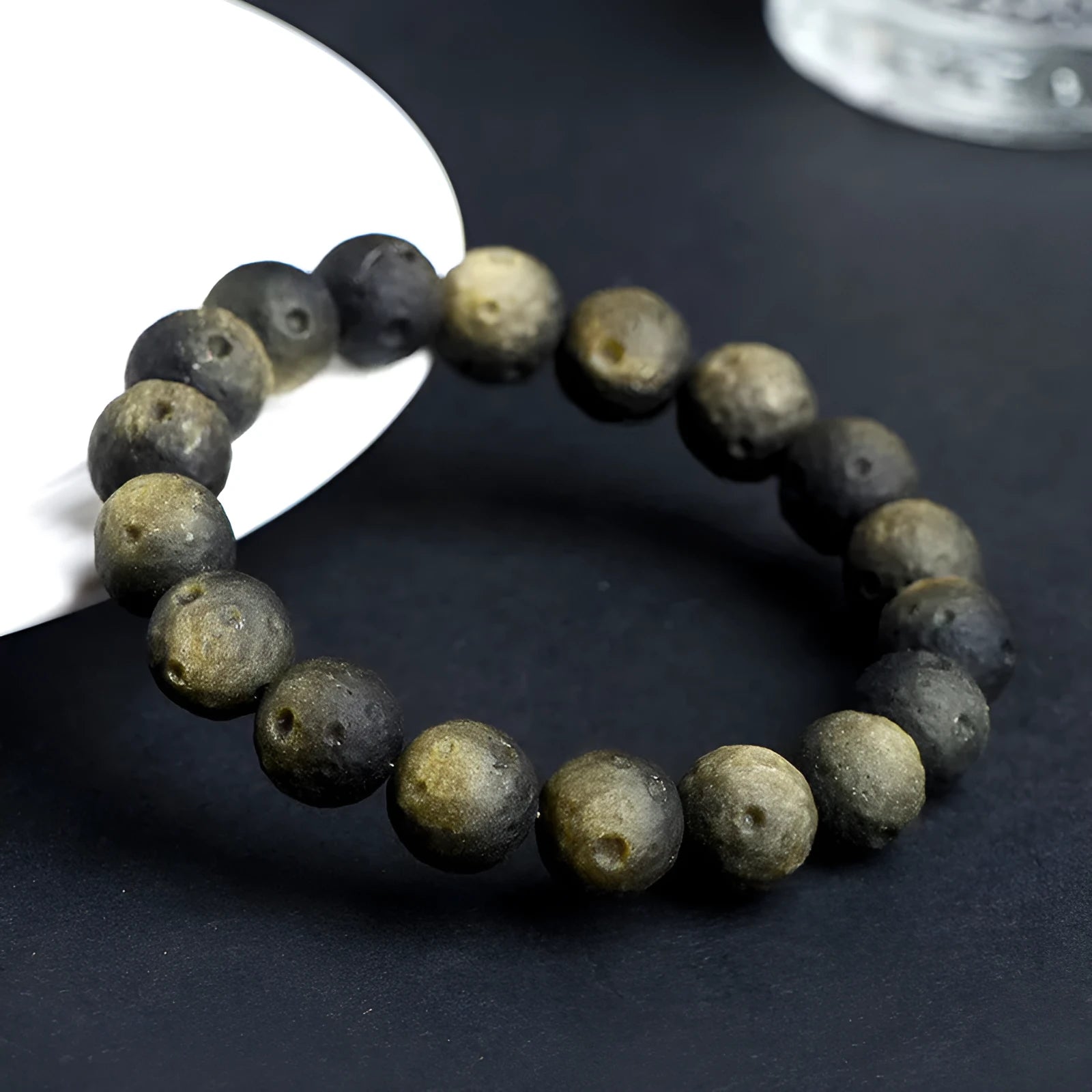 Natural obsidian crater ball bracelet in gold or silver finish on a wrist, showing textured bead detail.