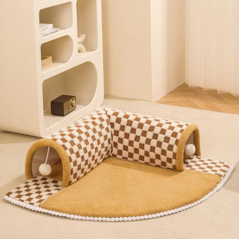 Brown plush plaid cat tunnel bed with a non-slip base on a wooden floor.