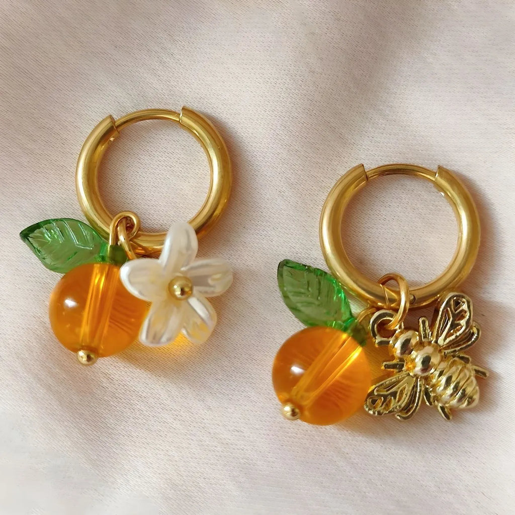 Pair of yellow acrylic sweet bee and honey fruit shaped earrings on a white background