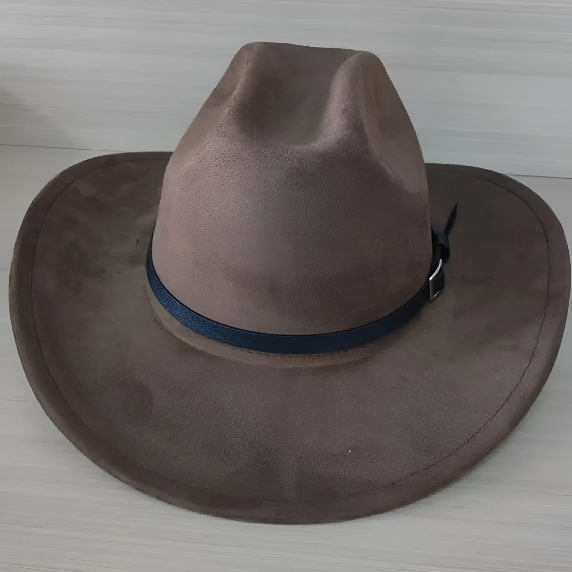 Brown leather velvet Western cowboy hat with curved edge and conical crown on wooden surface