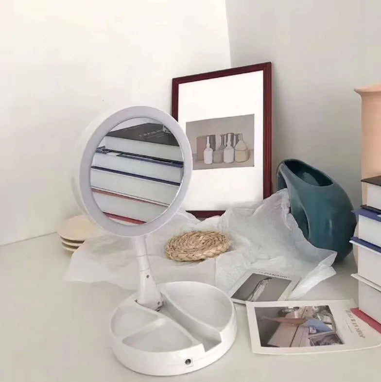 White foldable LED vanity mirror with USB charging port and built-in storage compartments on a table.