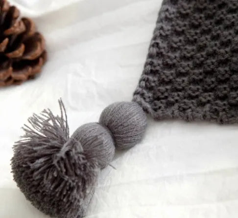 Plain beige knitted acrylic throw blanket with fringe on a grey sofa.