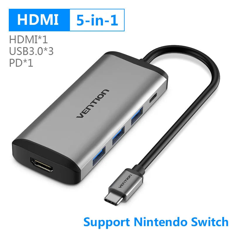 Deep grey USB-C to HDMI, USB 3.0, Ethernet, and card reader hub adapter on a desk.