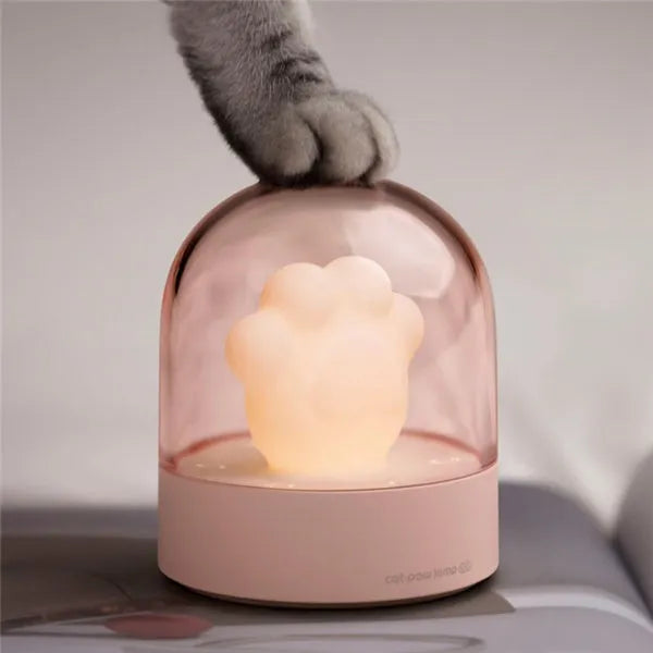 Grey and pink cat paw shaped USB night light with rotating lighting and music box features on desktop