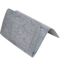 Felt bedside storage bag in beige with multiple pockets on a bed holding a remote control and book