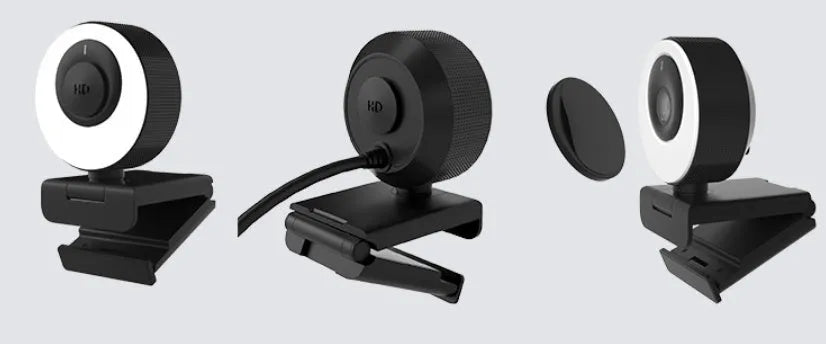 Black USB webcam with magnetic privacy cover on desktop next to computer monitor
