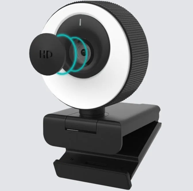 Black USB webcam with magnetic privacy cover on desktop next to computer monitor