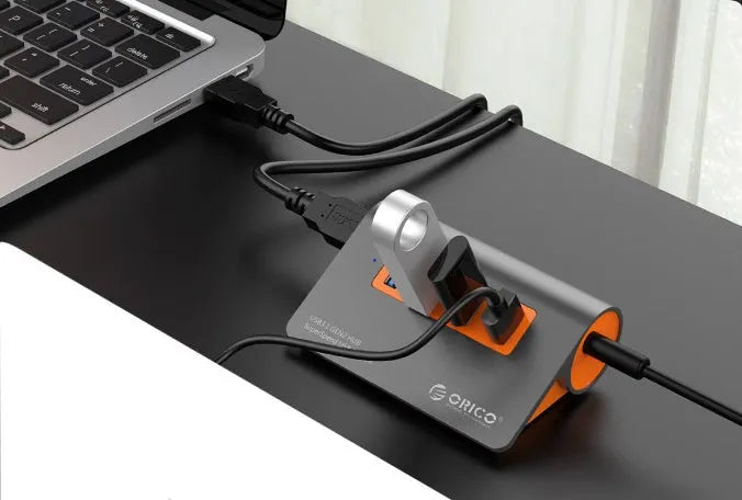 Dark grey aluminium USB-C hub with orange accents showing four USB 3.1 ports and separate data cable