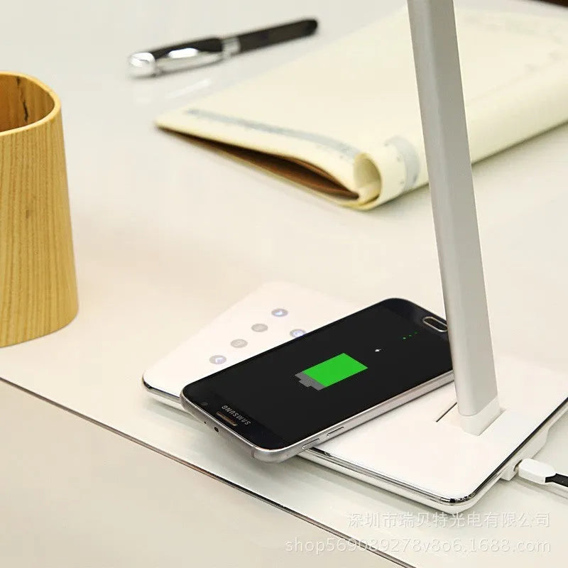 Black wireless charging LED desk lamp with touch control and USB cable on a wooden desk.