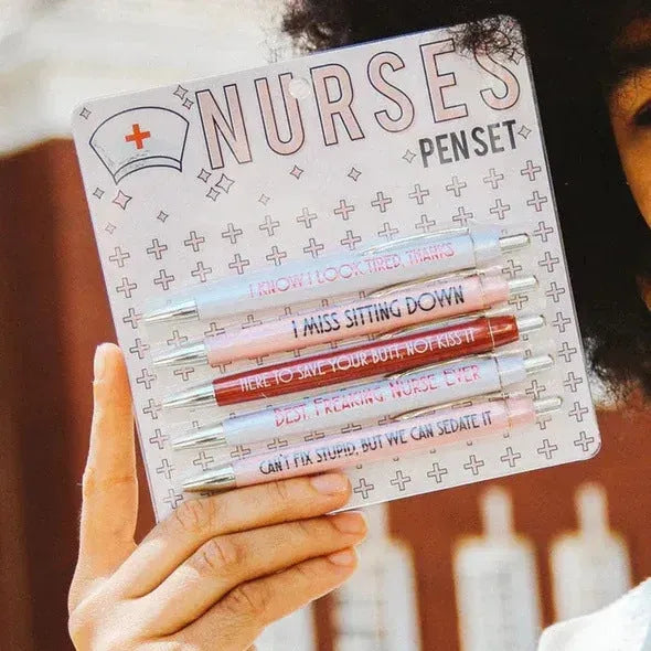 Set of five white plastic retractable ballpoint pens with blue and red nurse-themed humorous text printed on the barrels.