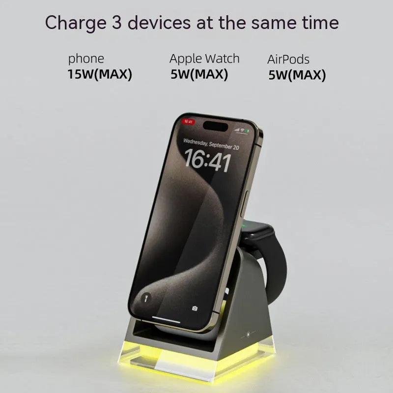 Black three-in-one magnetic wireless charger with night lamp charging phone, watch, and headset on a desk