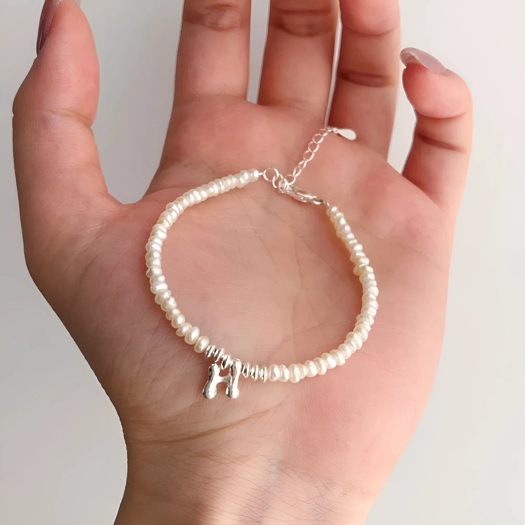 Women's natural freshwater pearl bracelet in 925 silver with letter shape charm on neutral background