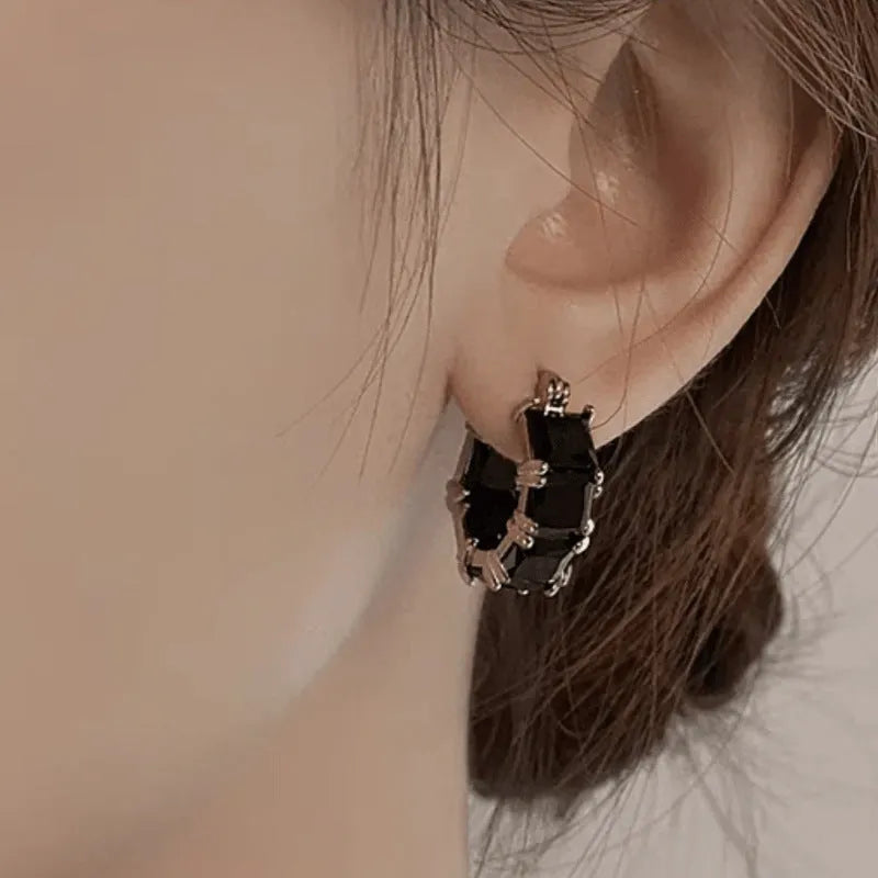 A pair of geometric U-shaped gold ear rings with round details and black zircon crystals.