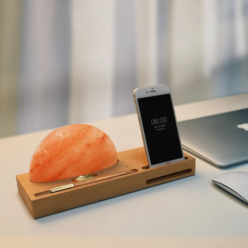Wooden base Himalayan salt lamp with wireless phone charging pad on top showing warm white glow.