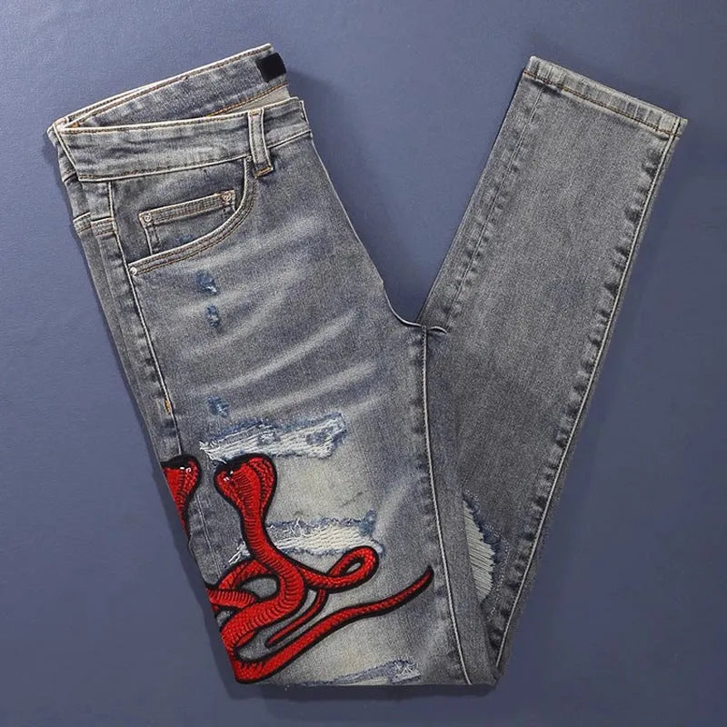 Slim fit light blue jeans with distressed knee patches, embroidery detail, and a faded wash.