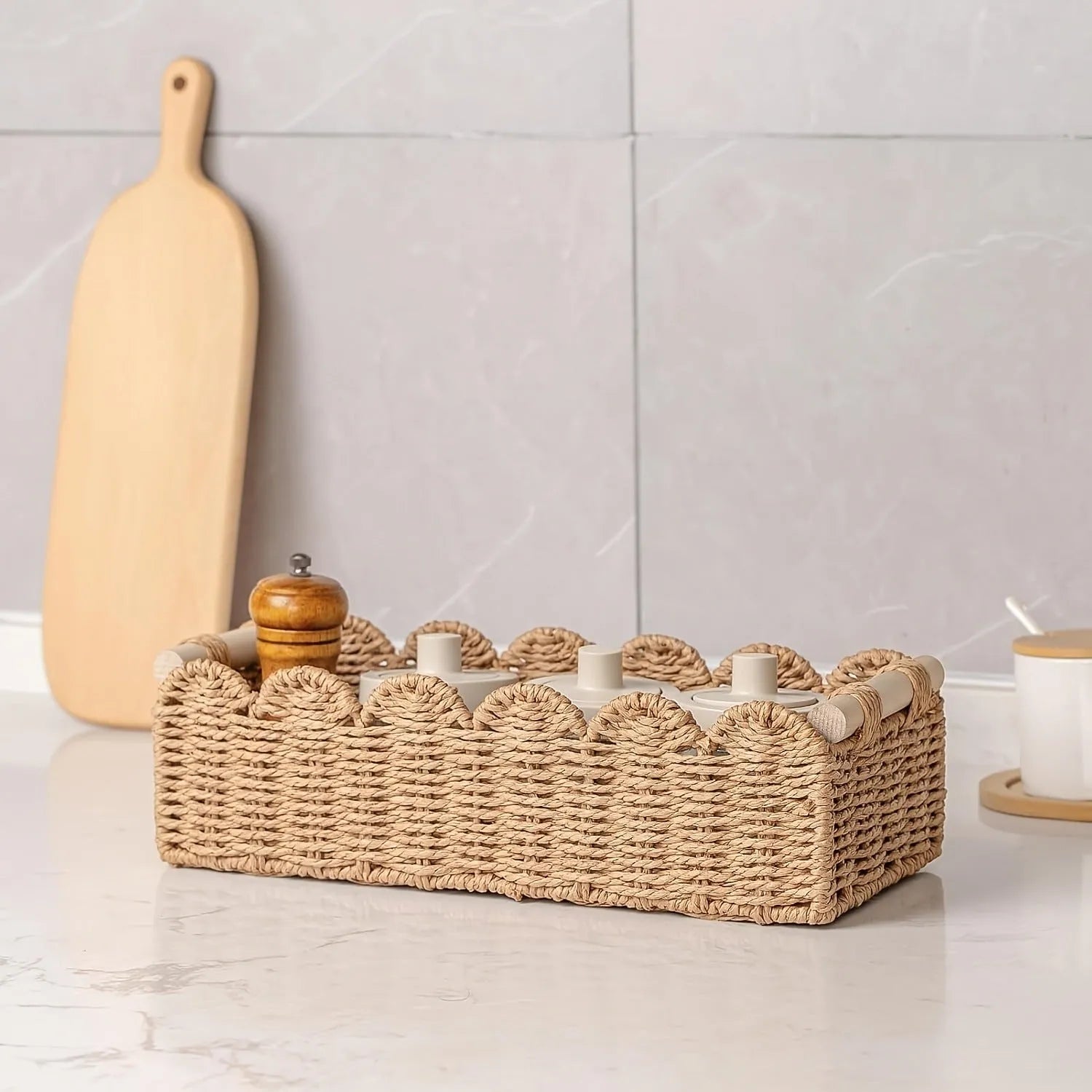 Modern woven rectangular storage basket in khaki colour on a wooden table holding remote controls and pens.