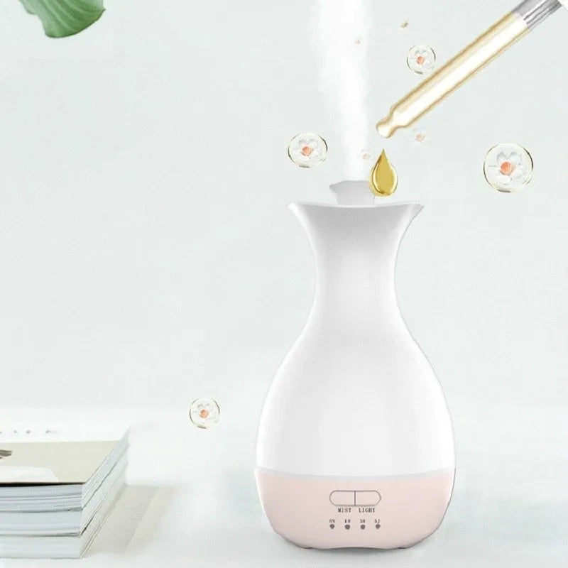 White or pink ultrasonic essential oil diffuser with water tank and multicolour LED night light on a table.