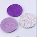 Three round grey cotton cord coasters on a wooden table