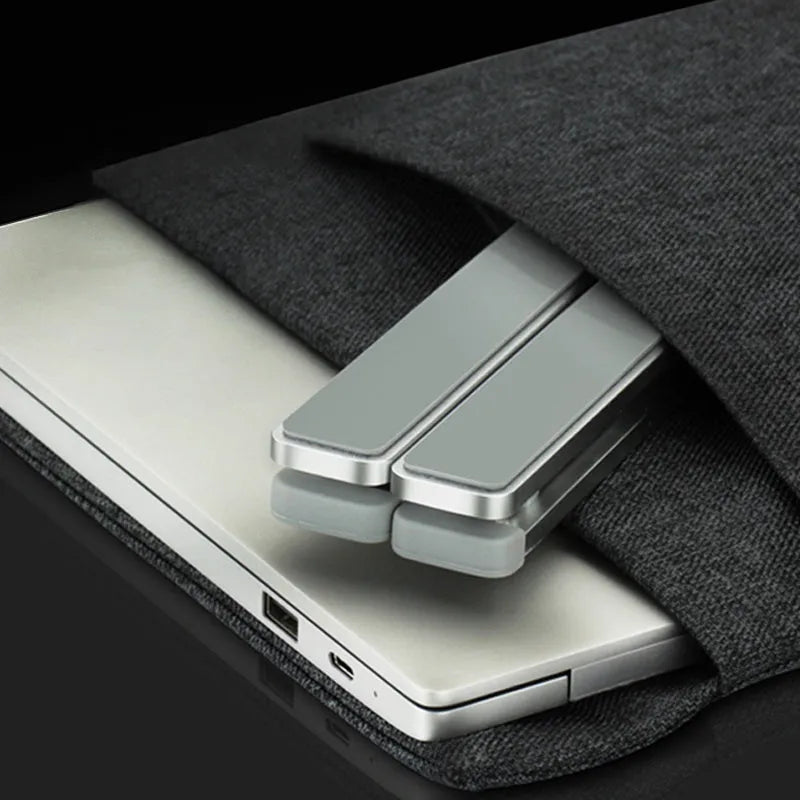 Adjustable folding laptop stand in silver, open on desk with laptop, showing hollow bottom and non-slip silicone pads