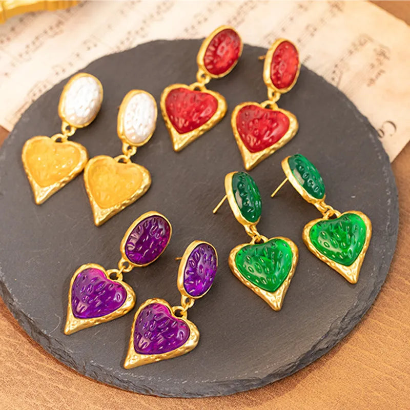 Close-up of oval love heart stud earrings with pleated needle posts in green, purple, red, and yellow-white colours.