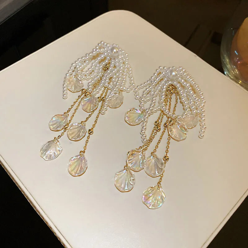 Gold long drop earrings with pearl, bow, tassel, and sequin detail on white background