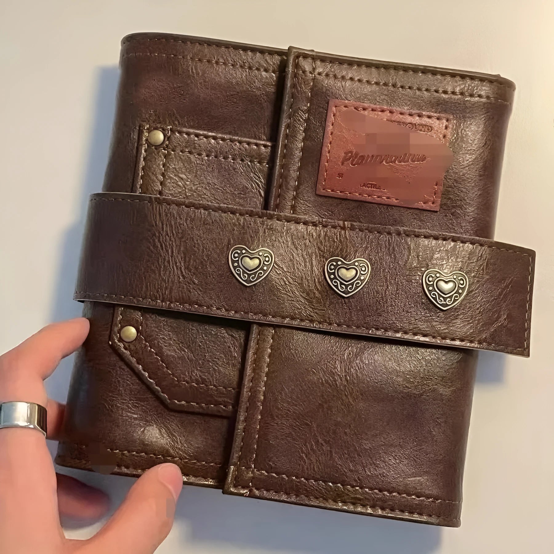 Brown A7 size notebook with a retro leather-look PU cover and metal buckle closure, lying open on a desk.