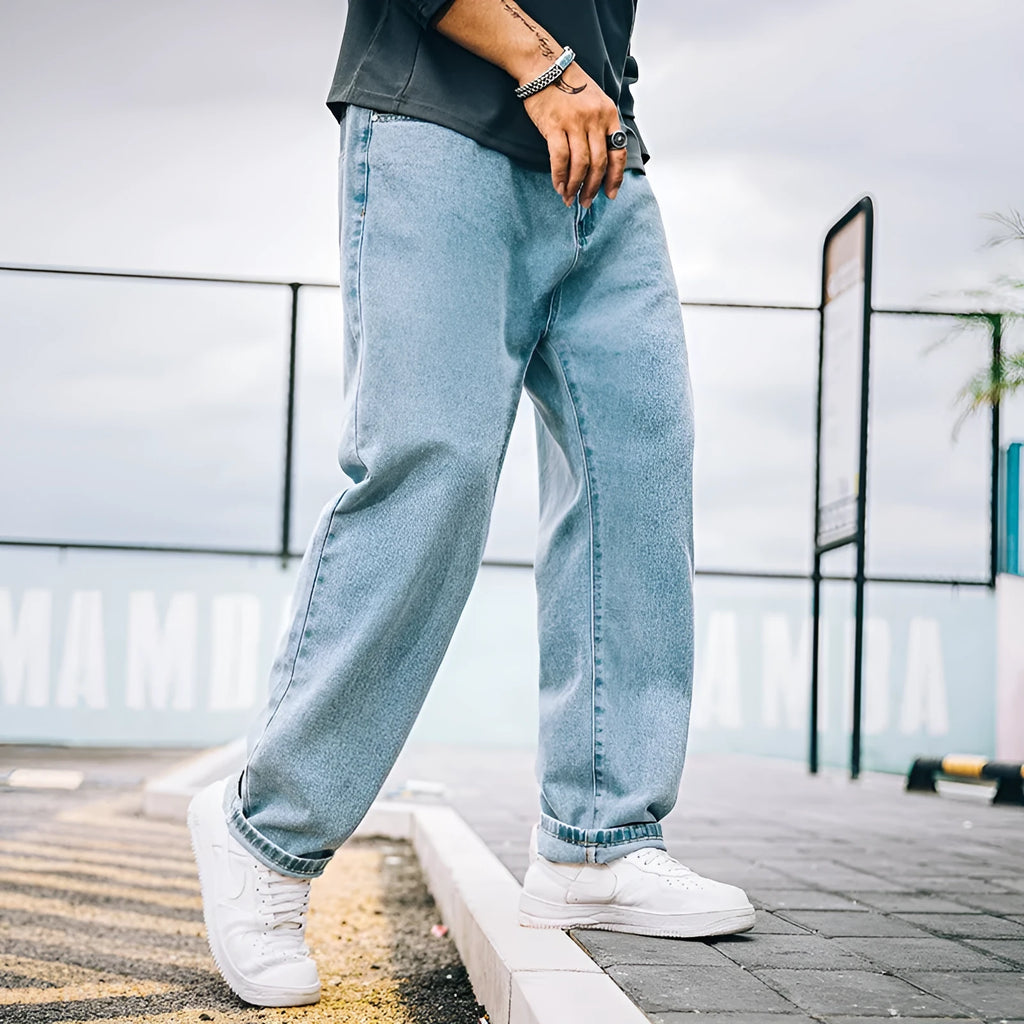 Man wearing dark blue loose straight leg cotton jeans with a mid waist and zipper fly.