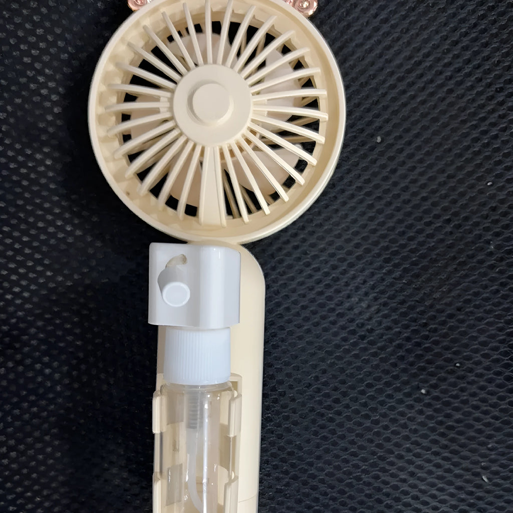 Compact plastic USB desk fan in apricot colour on a wooden desk surface.