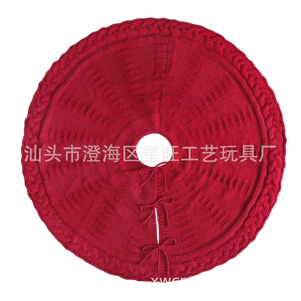 Red knitted wool Christmas tree skirt with 122cm diameter on floor under decorated tree