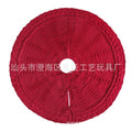Red knitted wool Christmas tree skirt with 122cm diameter on floor under decorated tree