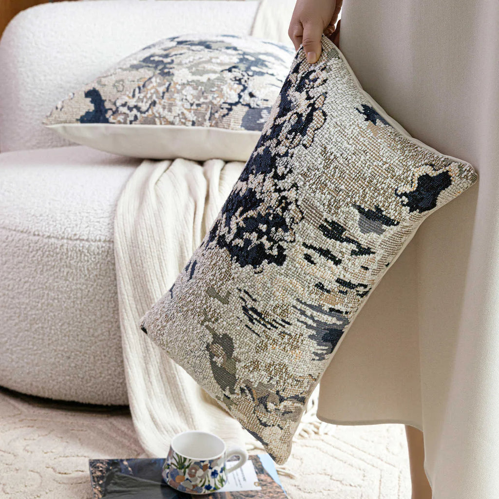 Antique blue square cushion with abstract botanical flower pattern on a grey sofa.