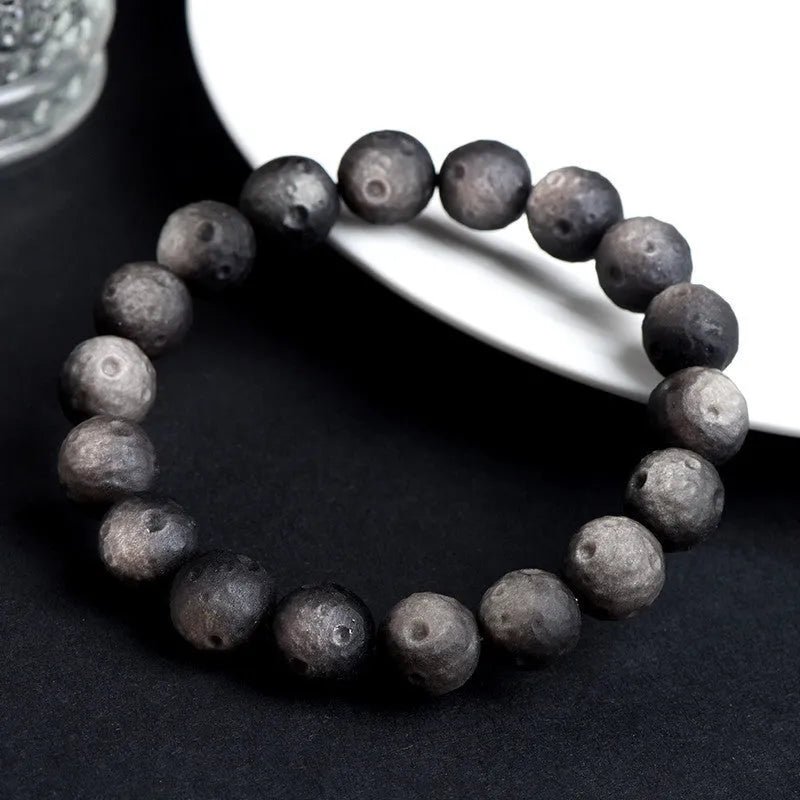 Natural obsidian crater ball bracelet in gold or silver finish on a wrist, showing textured bead detail.