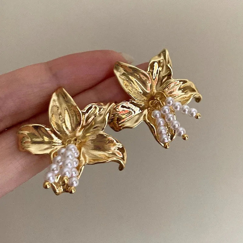 A pair of exaggerated gold metal flower earrings with pearl details, showing a niche jewellery style.
