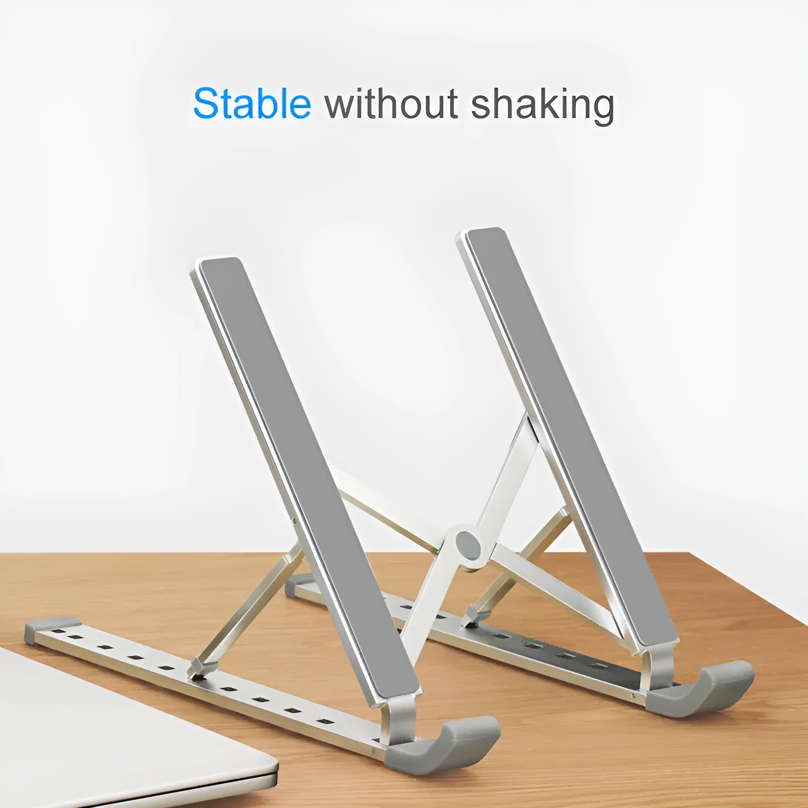 Adjustable folding laptop stand in silver, open on desk with laptop, showing hollow bottom and non-slip silicone pads
