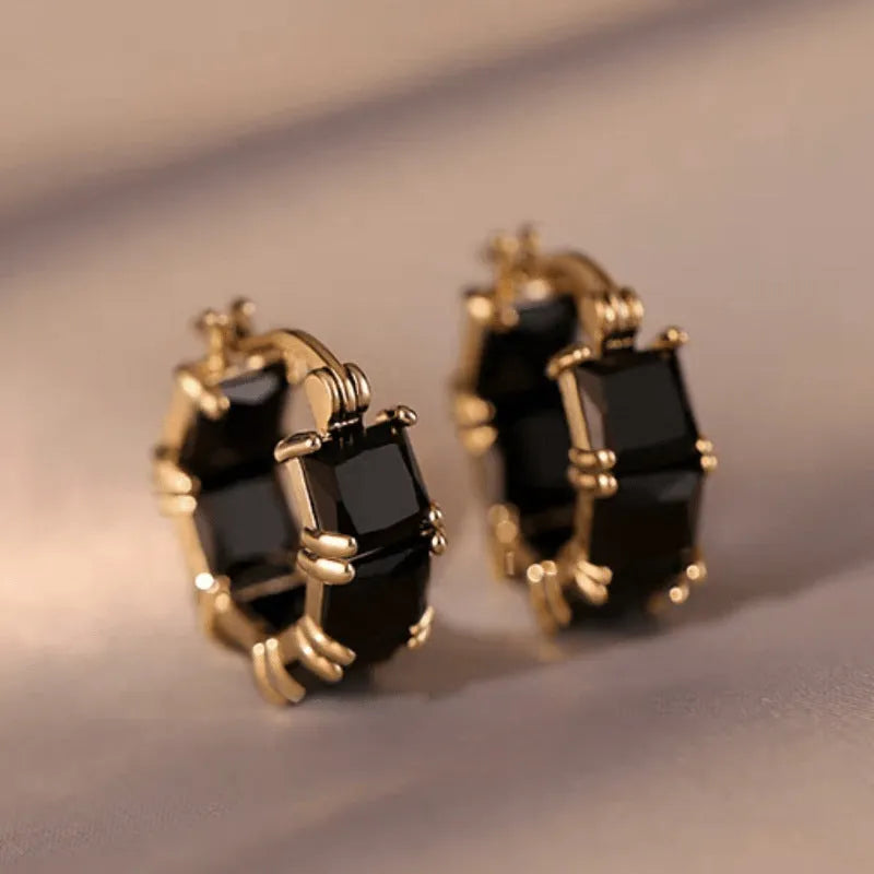 A pair of geometric U-shaped gold ear rings with round details and black zircon crystals.