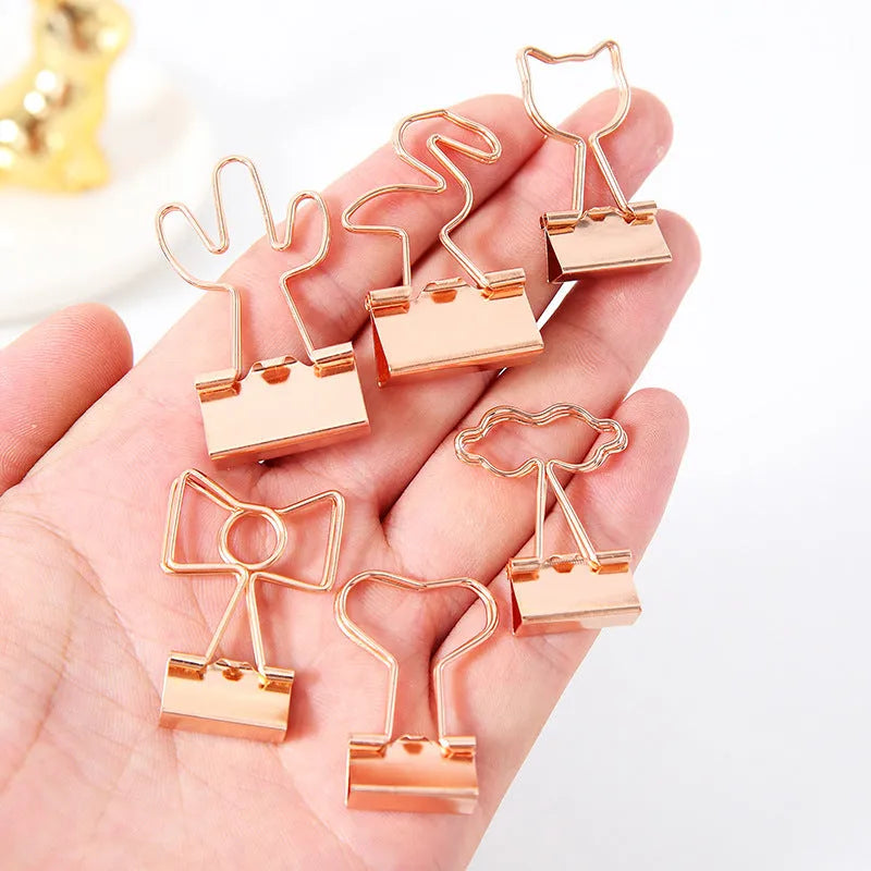 Gold metal decorative clip showing bow, cactus, cat, flamingo, and love shape designs.