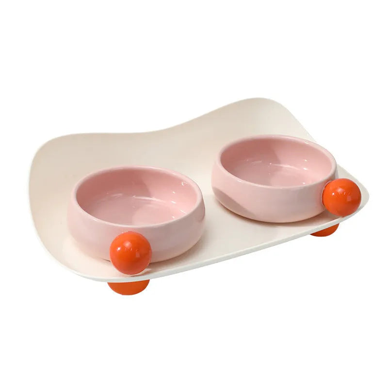 Pink and yellow elevated ceramic pet bowl set for food and water on a non-slip base.