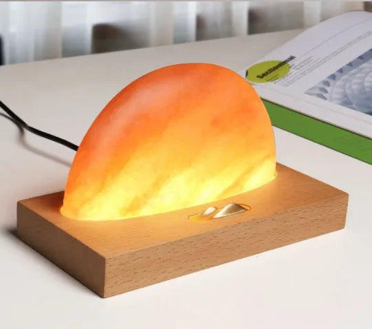 Wooden base Himalayan salt lamp with wireless phone charging pad on top showing warm white glow.
