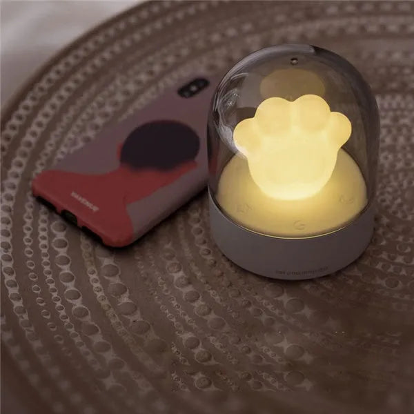 Grey and pink cat paw shaped USB night light with rotating lighting and music box features on desktop