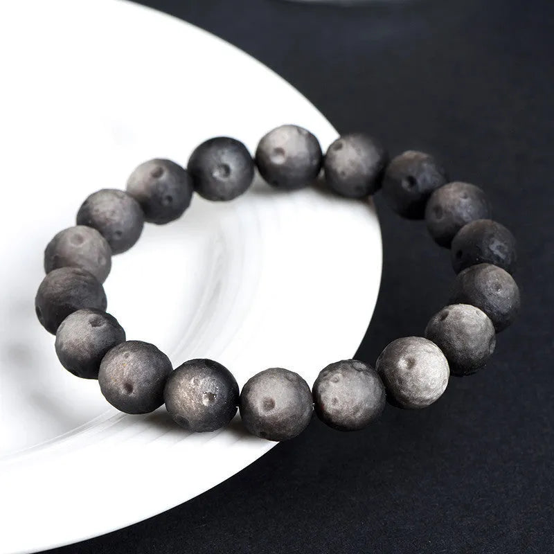 Natural obsidian crater ball bracelet in gold or silver finish on a wrist, showing textured bead detail.