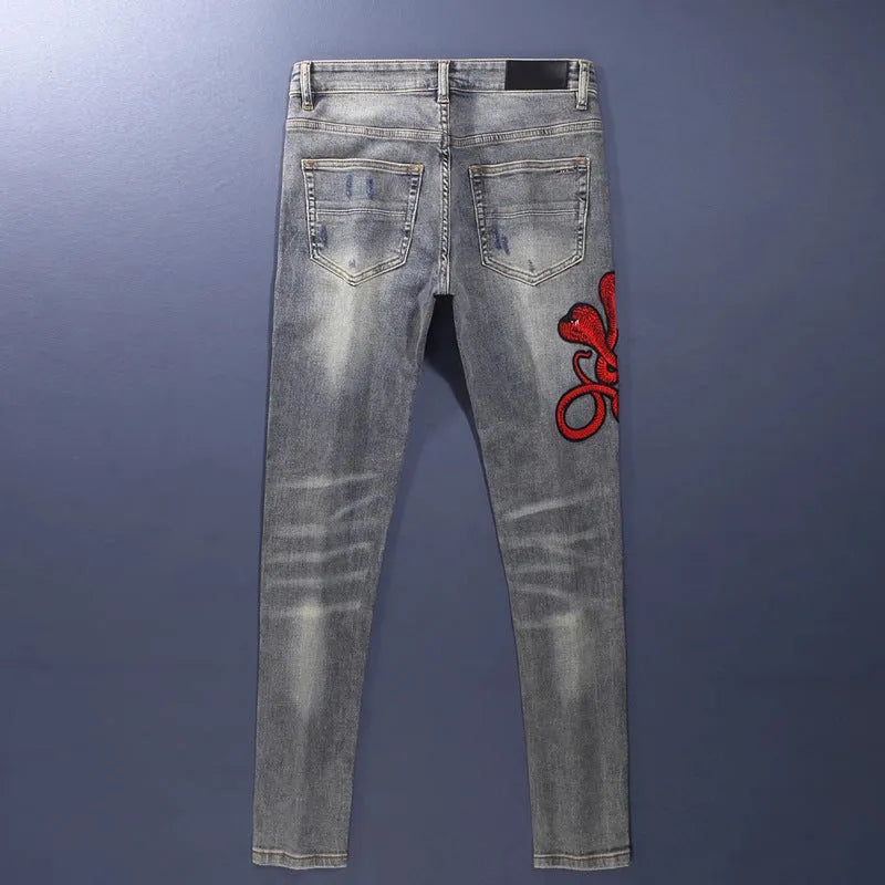 Slim fit light blue jeans with distressed knee patches, embroidery detail, and a faded wash.
