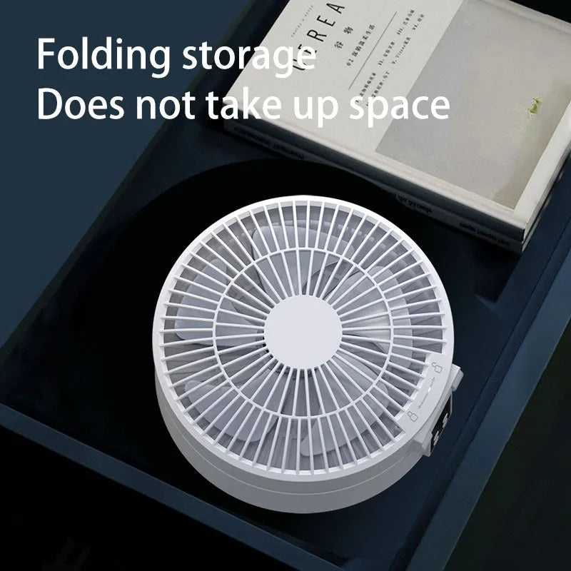 White portable folding fan with remote control on wooden desktop next to USB charging cable