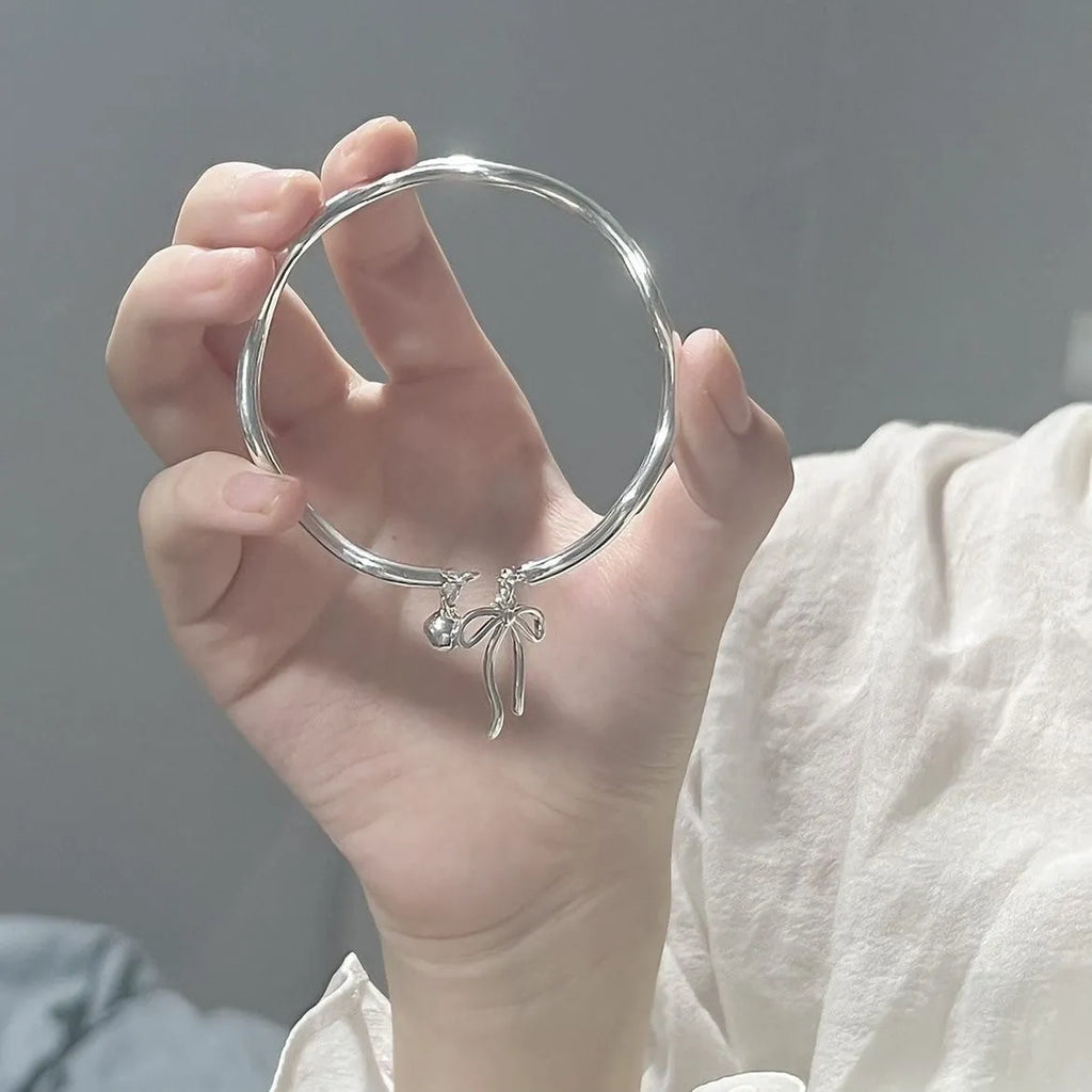 Close-up of an adjustable silver girlfriends bracelet with a bow-shaped bell opening clasp on a zinc alloy band.