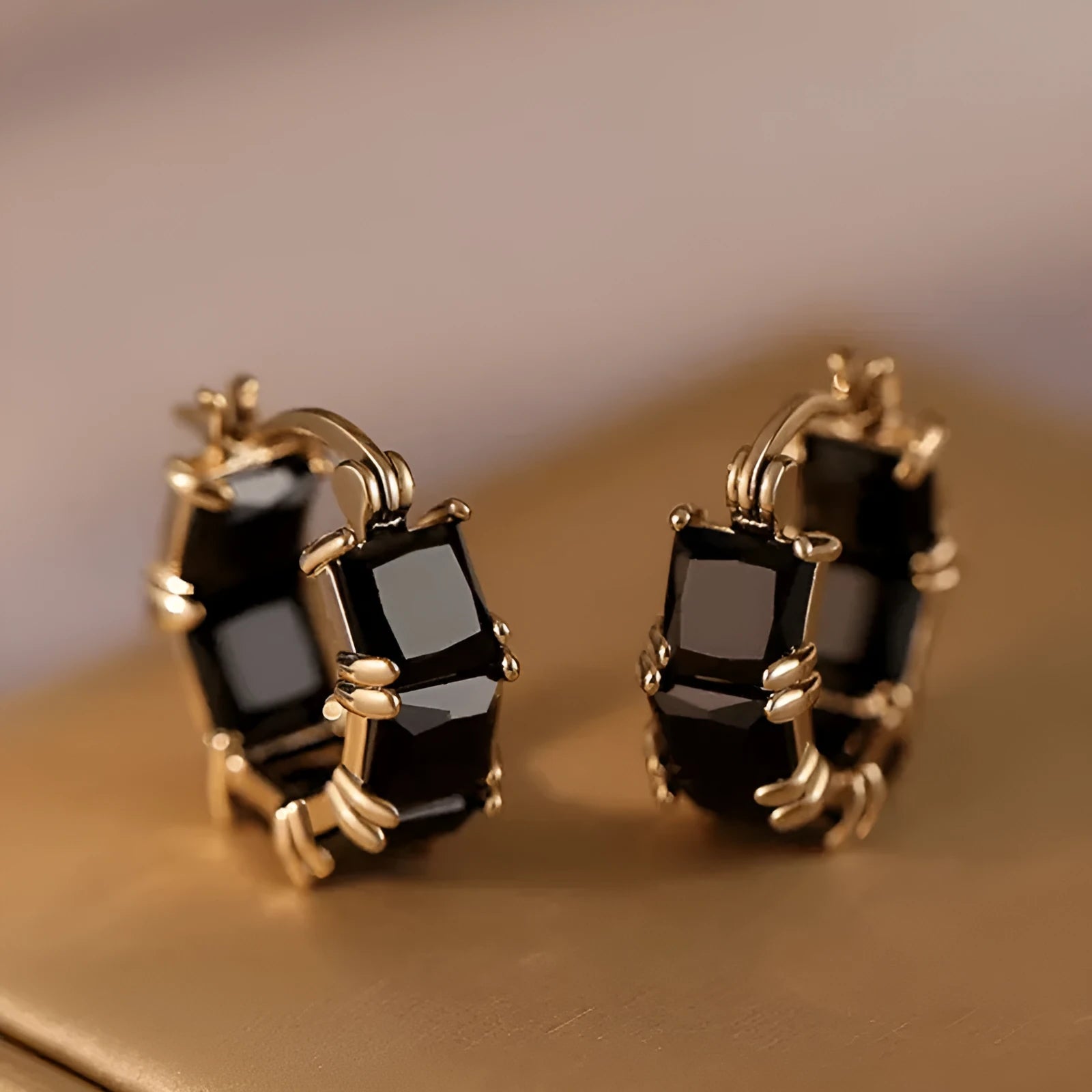 A pair of geometric U-shaped gold ear rings with round details and black zircon crystals.
