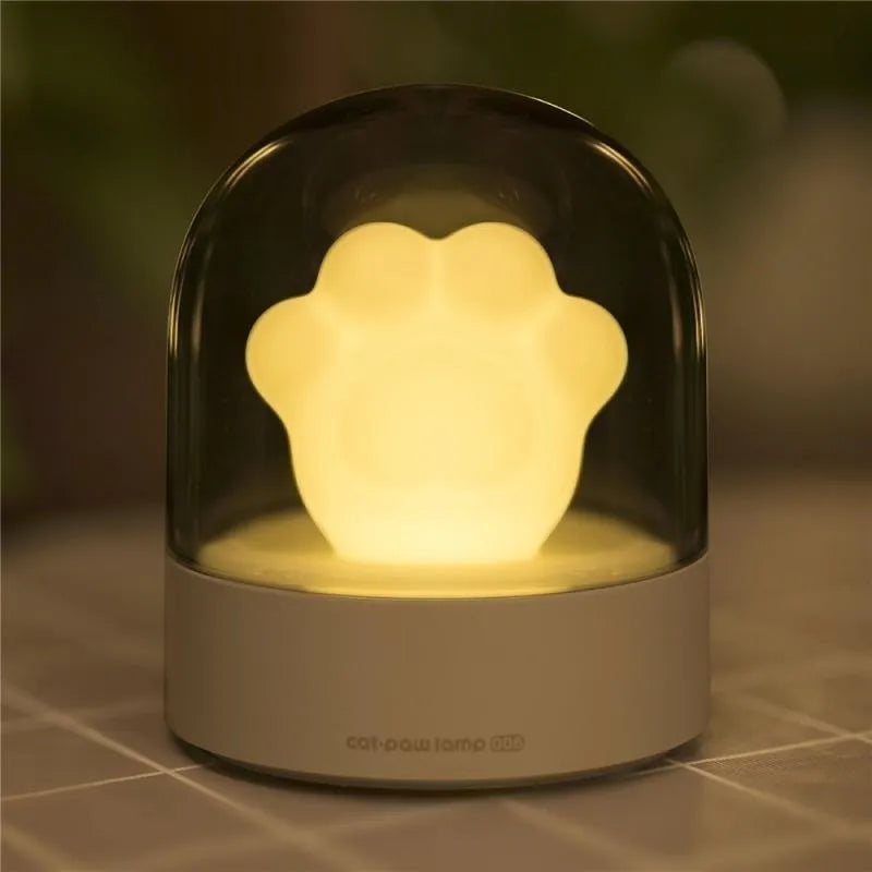 Grey and pink cat paw shaped USB night light with rotating lighting and music box features on desktop
