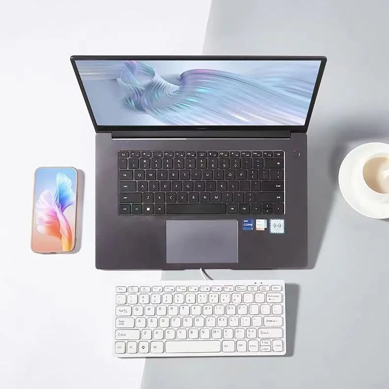 Compact wired USB keyboard in black, white, pink, or blue on a desk next to a laptop.