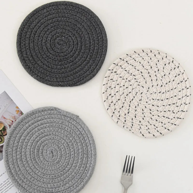 Three round grey cotton cord coasters on a wooden table