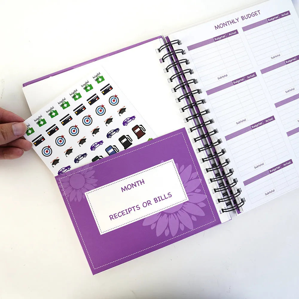 Purple coil-bound financial planning notebook with stickers, pen, and paper clips for monthly budget tracking