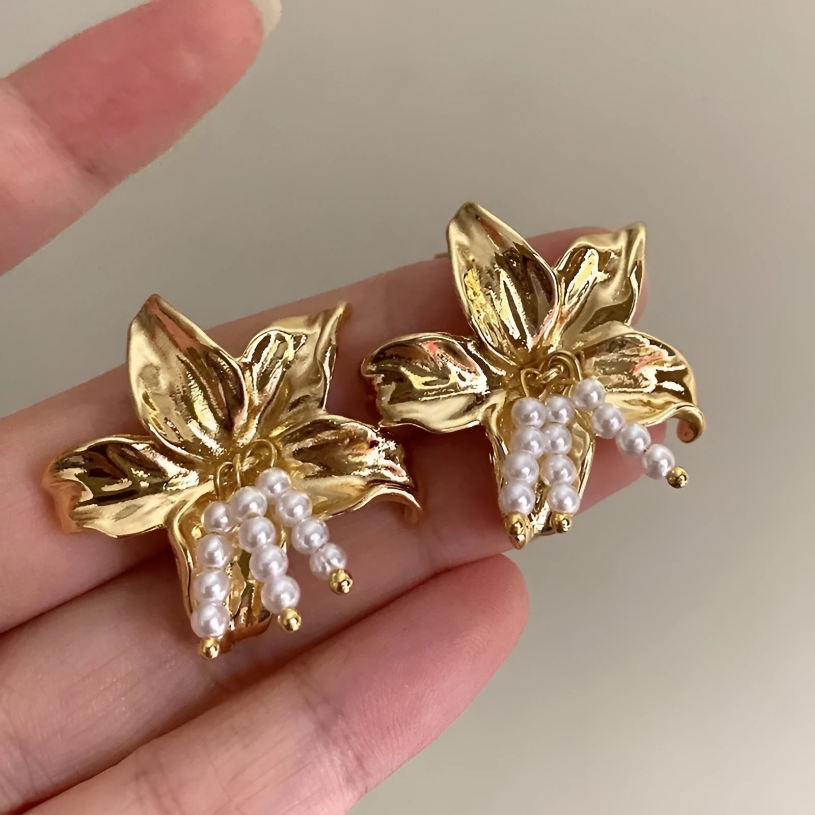 A pair of exaggerated gold metal flower earrings with pearl details, showing a niche jewellery style.